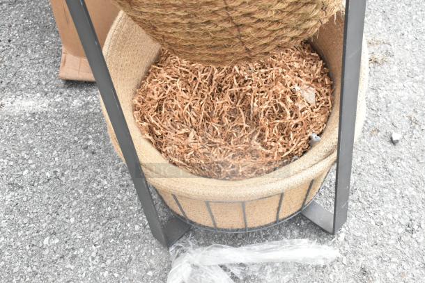 Metal stand with two round woven baskets, one filled with shredded packing material, on a gravel surface.