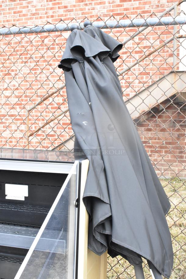 Two black patio umbrellas, folded and leaning against a fence. Minimal wear visible on fabric.