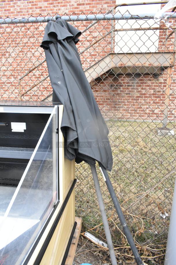 Two folded black patio umbrellas leaning against a fence, in used condition, with metal poles.