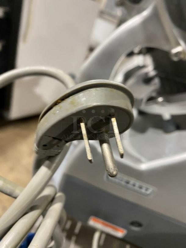 Hobart 2912 commercial electric deli slicer plug, showing prongs and body. Background shows slicer details.