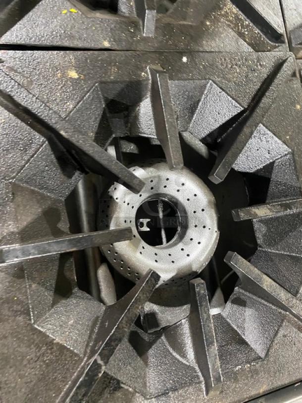 American Range 4-burner gas stove, stainless steel, commercial-grade, with wired oven rack, on casters. Close-up of burner.