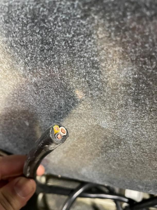 Close-up of a cut power cord held in front of a textured surface. The wires are exposed, showing three internal cables.