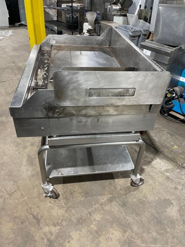 WoodStone 48" stainless steel gas-powered plancha griddle with back/side splash, undershelf stand, on casters. SN: GP1B16MAY1704992.