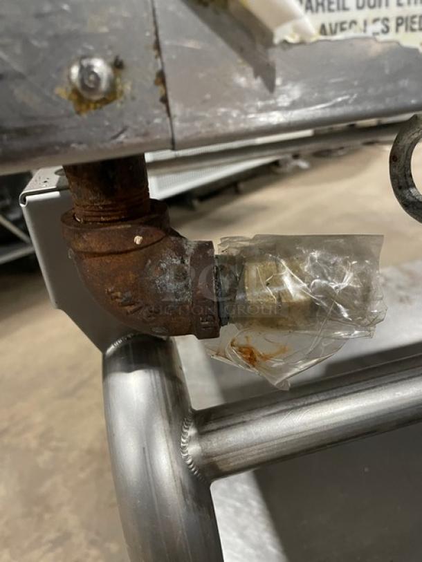 WoodStone stainless steel gas-powered plancha griddle underside showing gas connection, lightly rusted, on cart base.