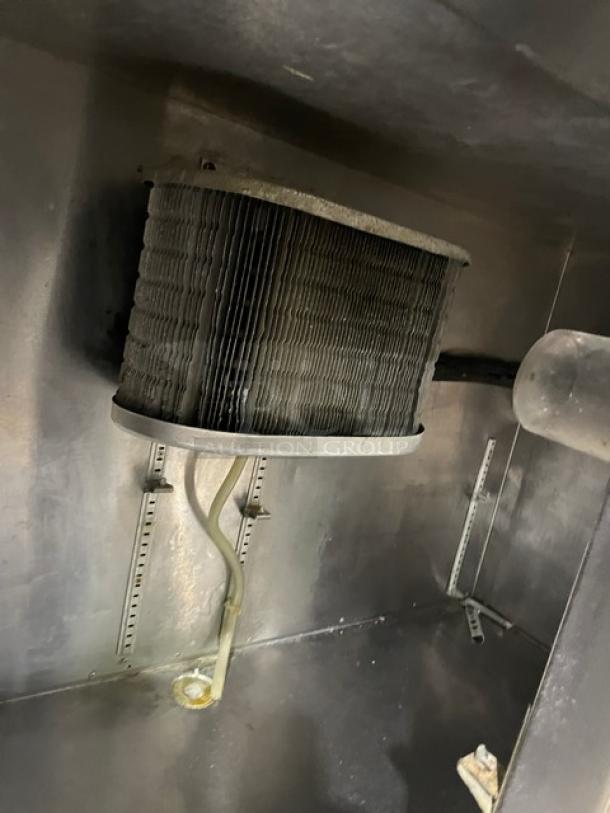 Commercial stainless steel refrigerated worktop station interior, featuring visible cooling coil and piping.