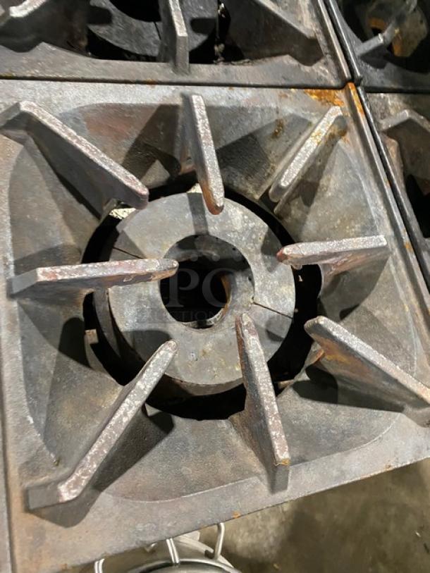 Bakers Pride gas-powered 10-burner range with back splash, overhead salamander shelf, and oven racks. Rust present.