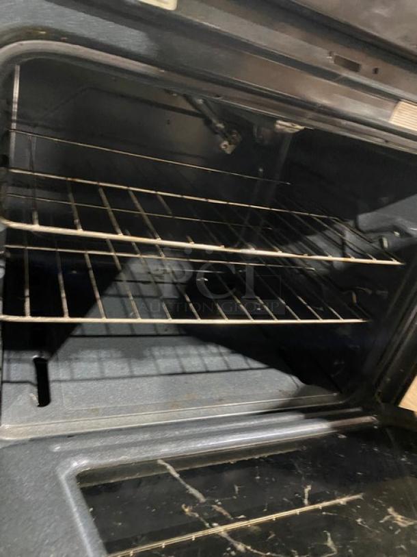 Stainless steel Amana commercial gas range/oven combo with 4 burners, digital controls, and wired oven rack, open door view.