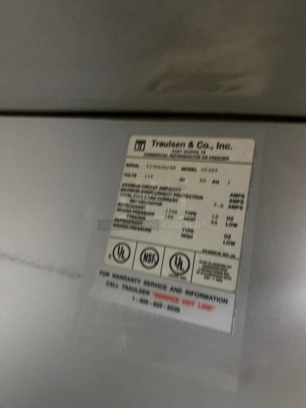 Label on Traulsen UC2HT commercial refrigerator showing specs: Model UC2HT, SN: T276920J98, 115V, 1 Phase, on legs.
