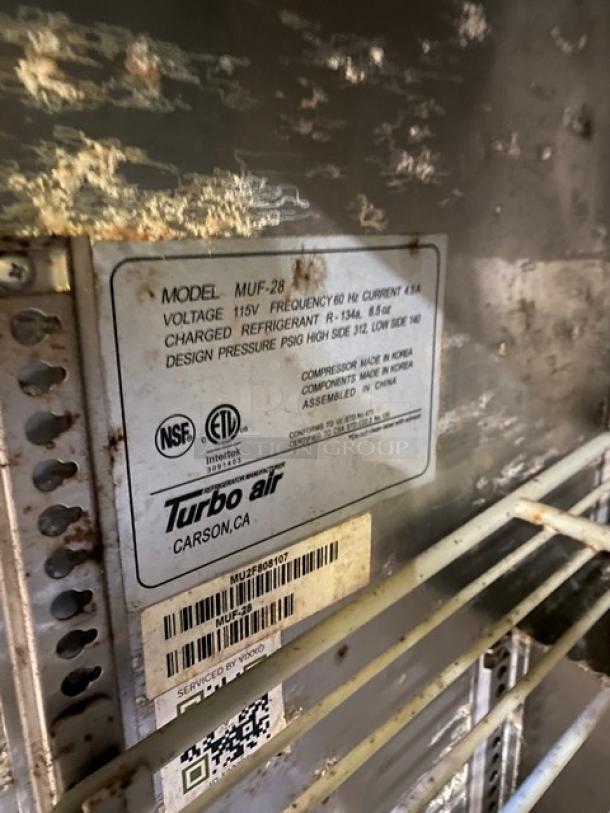 Close-up of inside a Delfield Commercial Stainless Steel Undercounter Refrigerator, showing a coated wire rack and a label detailing model and voltage specifications. Model 406CA-DHL-DD1. 115V, on casters.