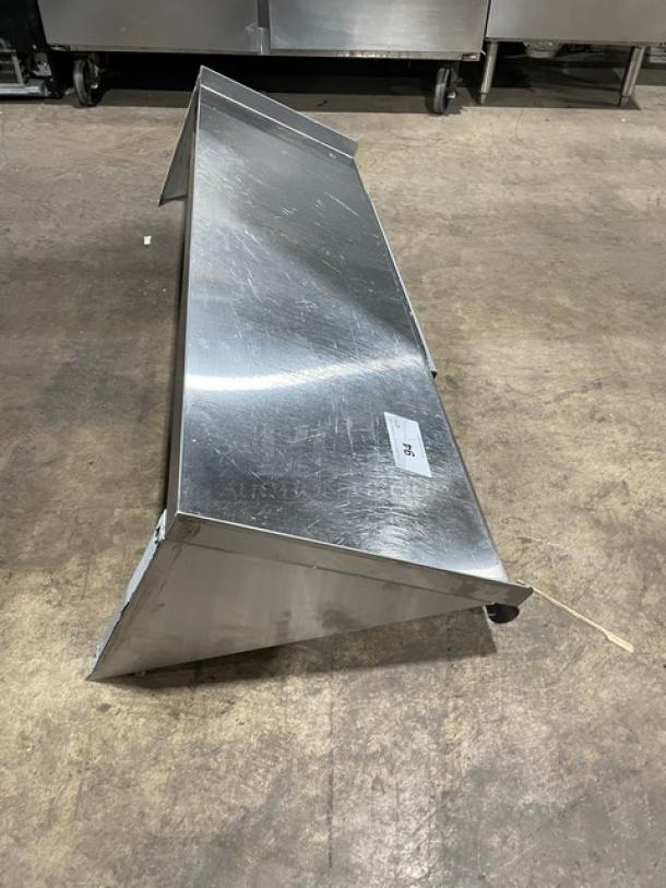 Commercial stainless steel rectangular wall-mount shelf, includes ticket/order holder, visible surface scratches, durable construction.