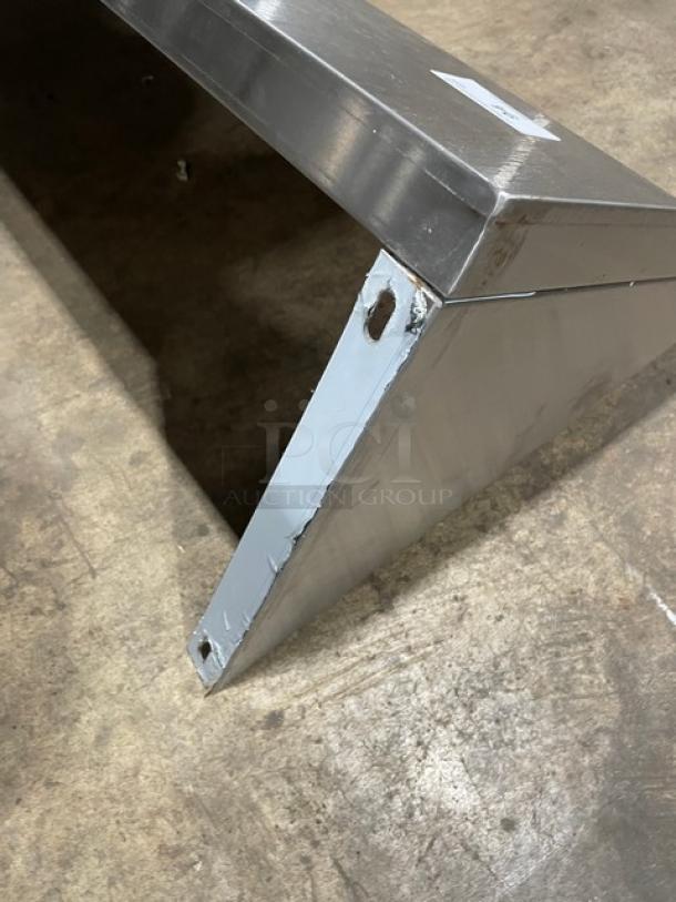 Commercial stainless steel wall-mount shelf with ticket/order holder, rectangular, used, visible mounting holes.