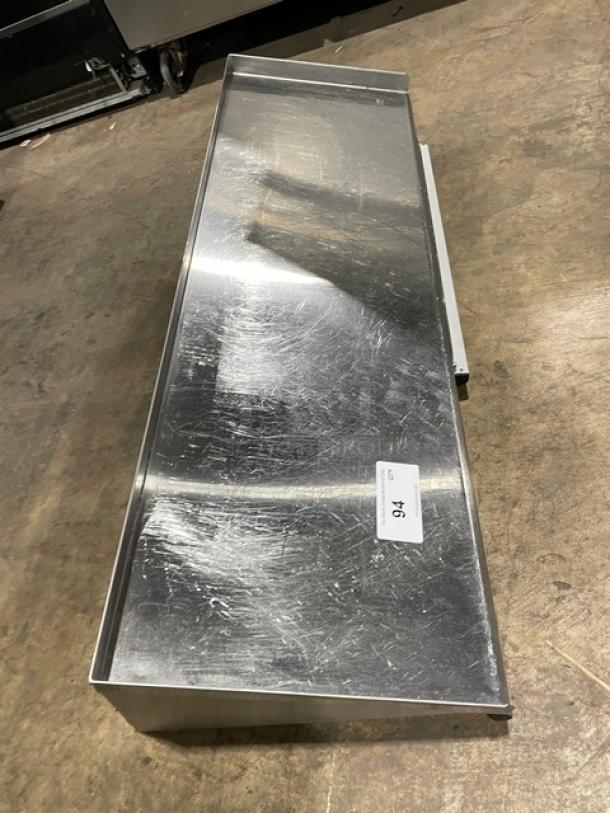 Commercial stainless steel wall-mount shelf, rectangular, with ticket/order holder. Lightly scratched surface, durable.