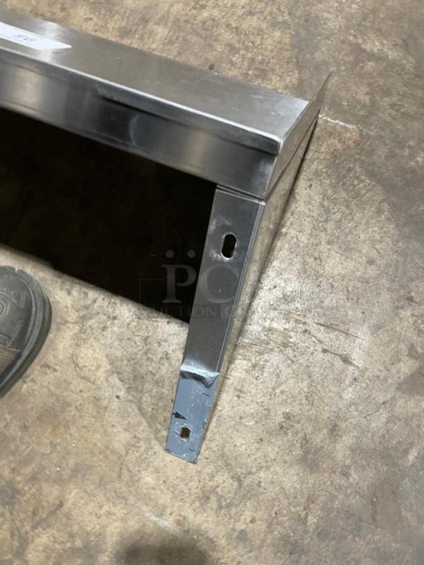 Commercial stainless steel rectangular wall-mount shelf, sturdy design, visible mounting holes, used condition with some wear.