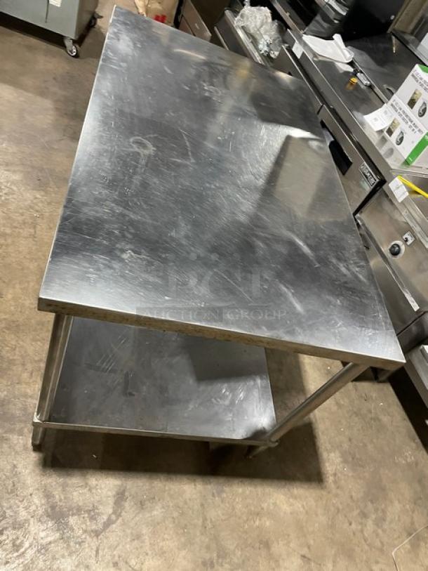 Commercial stainless steel flat worktop table with single undershelf on legs, showing minor surface wear, ideal for kitchen use.