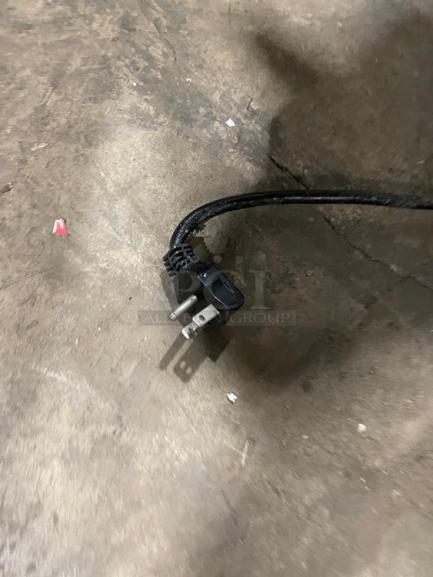 Power cord on concrete floor, possibly for Arctic Air refrigerated chef base. Black three-prong plug.