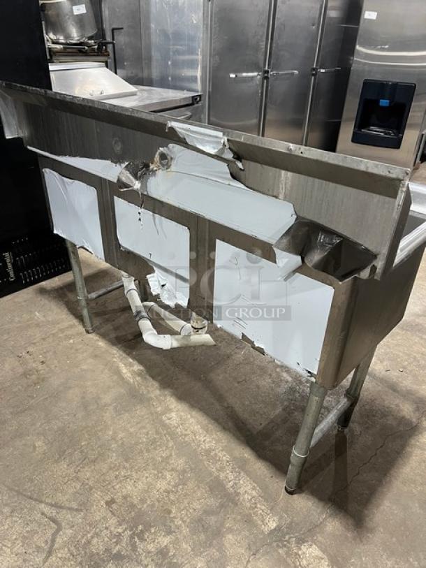 KCS Commercial stainless steel 3-compartment sink with backsplash, on legs. Visible wear and piping underneath.