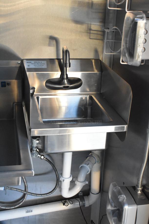 Stainless steel hand sink with faucet inside a brand new 2021 Cruising Kitchens Burger King trailer, showing piping and fixtures.