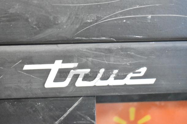Close-up of a "True" logo on a 2019 GDM-41SL-48-HC-LD cooler, showing minor surface scratches.