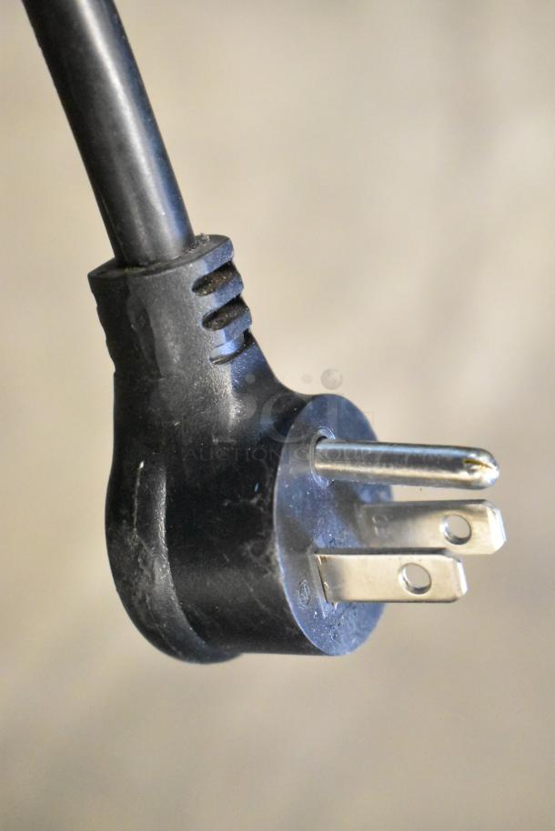 Close-up of a black electrical plug, likely part of a True GDM-08-HC refrigerator, showing prongs and cable in clean condition.