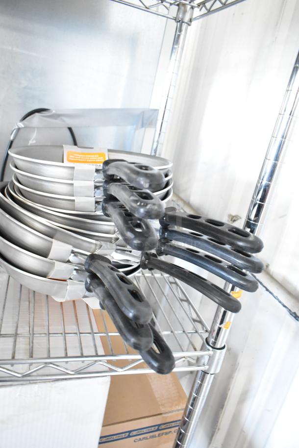Stack of Vollrath 67810 skillets on a shelf, new condition, black handles, part of 14-item auction lot.