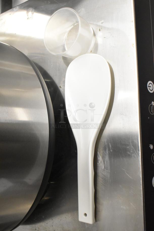 Brand new Galaxy 177GRCS60 60-cup electric rice cooker parts, includes plastic spatula and measuring cup, on metallic surface.