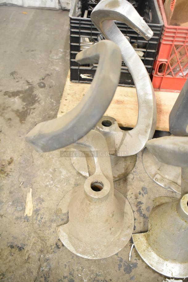 Six various dough hook attachments for mixers, metal, slightly worn condition, piled on a concrete surface.