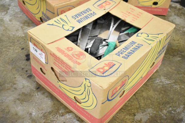 A box containing 150 sharpened stainless steel knives, including chef knives, visible in a repurposed Dole banana box.