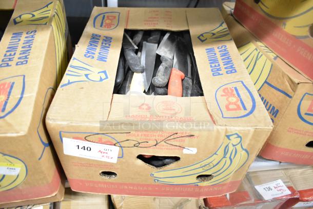 Box of 150 sharpened stainless steel knives, including chef knife, in reused banana boxes. Variety of handle colors visible.