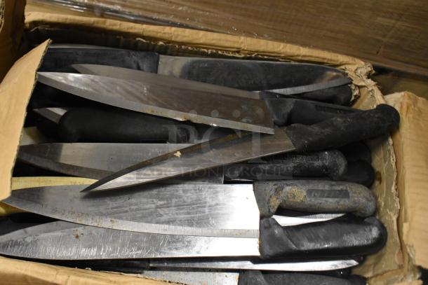 85 sharpened stainless steel knives, including chef knives, in a cardboard box. Black handles show wear.