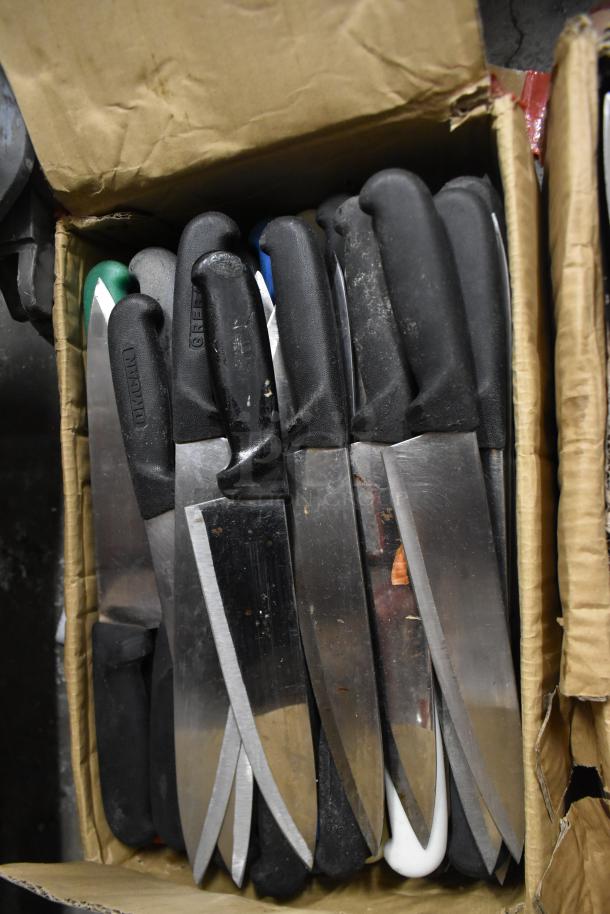Cardboard box with 85 sharpened stainless steel knives, black handles, including chef knives. Markings indicate brand names.