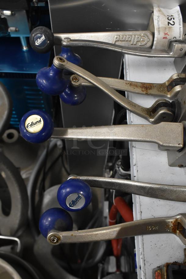 Seven Edlund commercial can openers with mounts, featuring metallic handles and blue grips, showing some rust marks.