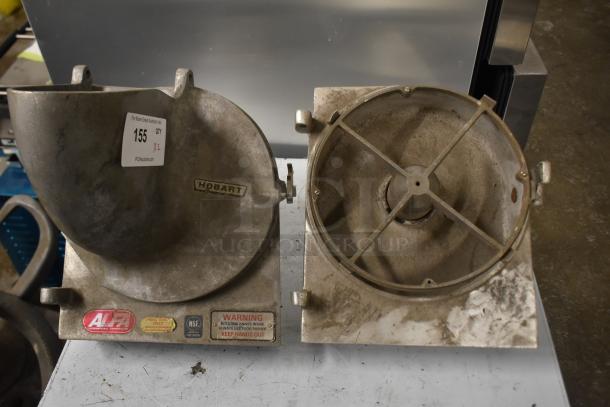 Two Hobart pelican heads with slicing blade frame, one missing front piece and blade, shows wear, safety labels visible.