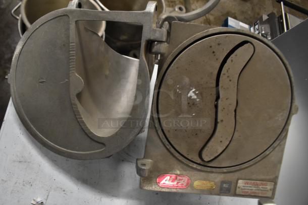 Two metal pelican heads with slicing blade and blade frame, one missing front piece and blade, visible labels and warning tags.