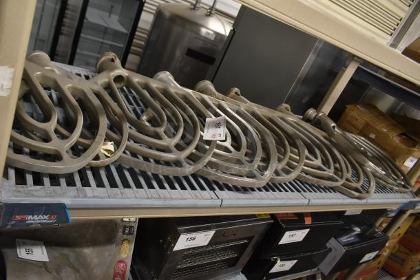 Nine metal paddle attachments for Hobart mixer on a shelf, each tagged, in used condition.