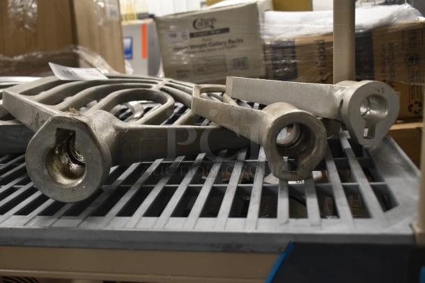 Nine Hobart mixer paddle attachments, metal, various designs, used condition, on a metal rack.