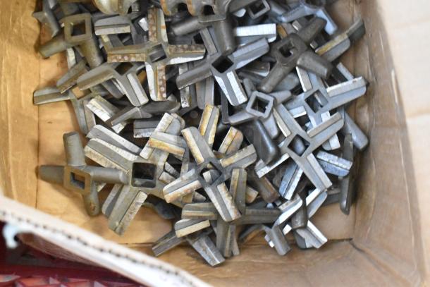 Box containing 53 various steel meat grinder knives, showing wear and rust. Square center holes for attachment.