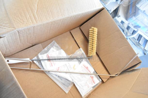 Box containing cleaning brush and wrapped items next to labeled packets, likely cleaning supplies for a Frymaster fryer.