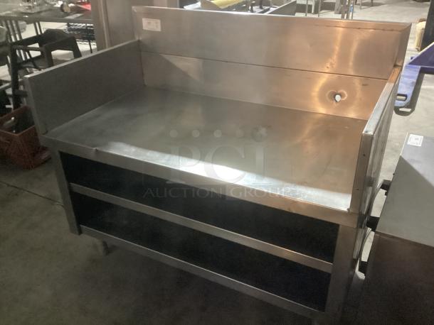 Low-rise stainless steel base with backsplash, measuring 48 x 27 x 42 inches. Features dual open shelves, pre-owned condition.
