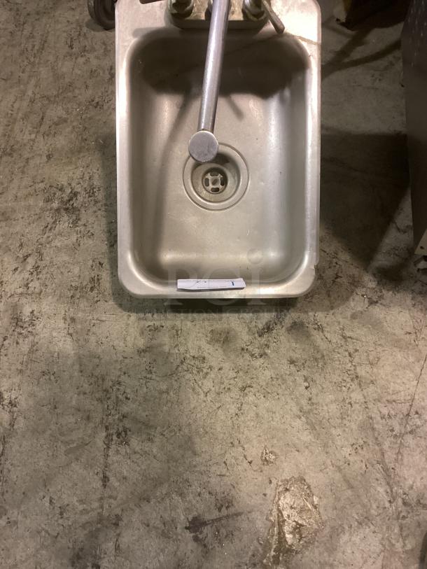 Stainless steel hand sink with faucet, 12x18 inches, in good condition. Drain plug and plumbing fixtures visible.