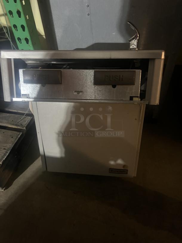 Stainless steel water fountain with two push buttons, in fair condition, featuring a chrome spout and slight wear.