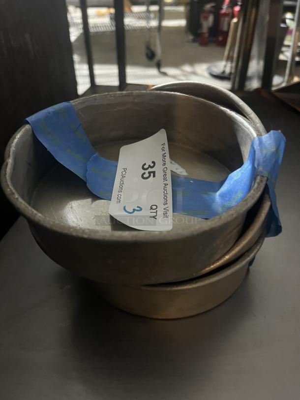 Set of three 7-1/4” cake pans in used condition with an auction label indicating quantity 3.