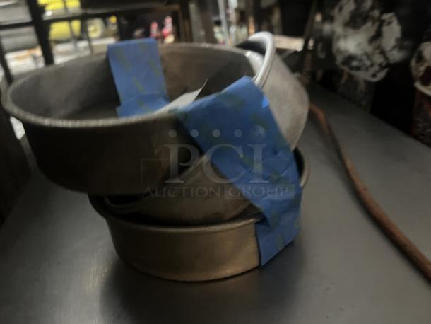 Three 7-1/4” cake pans stacked, secured with blue tape, showing moderate wear.