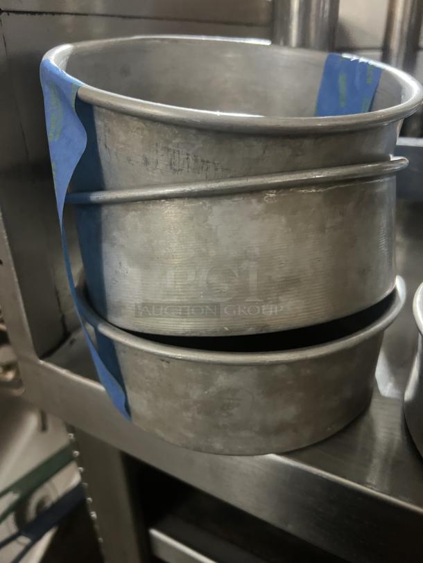 Stack of three used 7-1/4” metal cake pans with visible wear, featuring blue tape for identification.