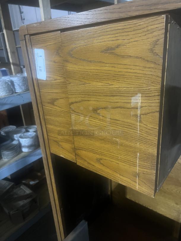 Wood desk with oak finish, side panel visible. Shows minor surface wear. Tag visible with number 87.