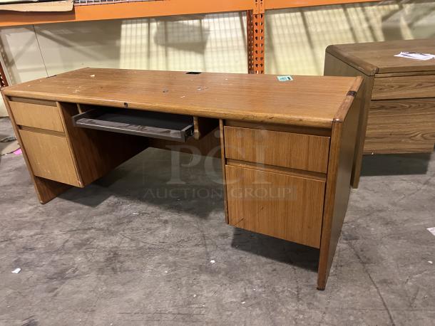 Wood desk with dual side drawers and a central keyboard tray. Shows signs of wear, surface scratches visible. Sturdy condition.