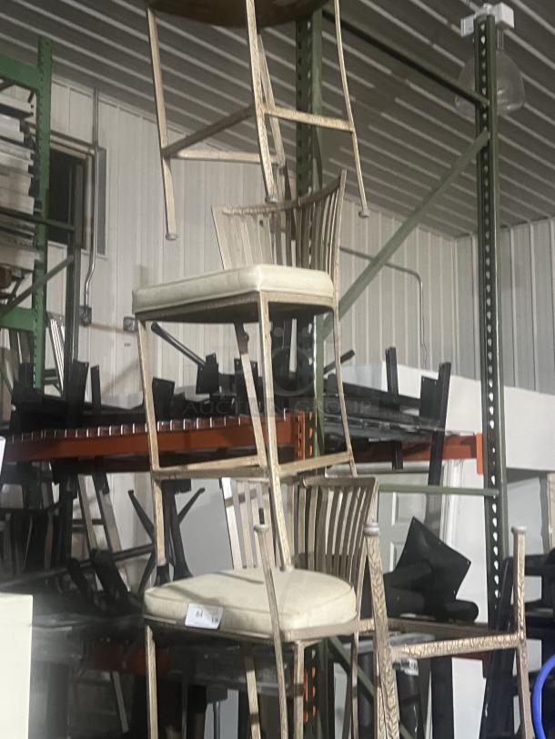 Two wrought iron style barstools with cream cushions, patio design, rustic finish; stacked in storage.