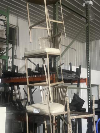 Two wrought iron style barstools with cream cushions, patio design, rustic finish; stacked in storage.