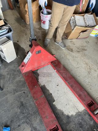 Red pallet jack with visible wear, labeled "6600 LBS," sturdy metal construction, stored in a garage setting.