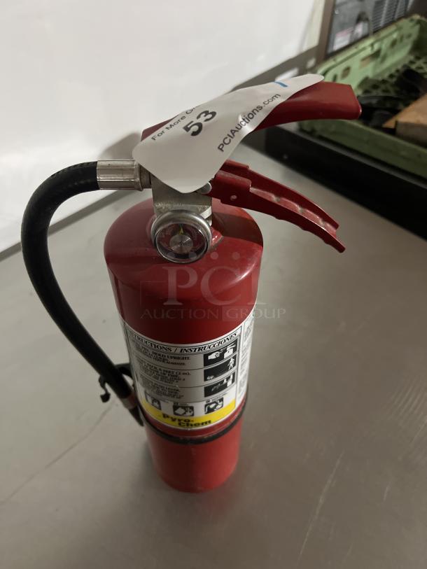Red fire extinguisher with hose and pressure gauge, labeled "Pyro Chem." Auction tag "53" is attached to the handle.