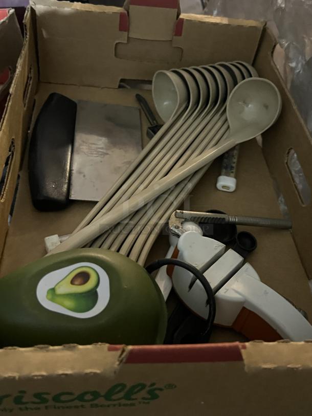 Box of assorted kitchen utensils, including measuring ladles, can opener, and scraper. Appears used. Green item with avocado sticker.